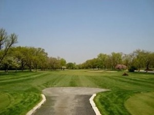 A view of a well-maintained golf course pathway leading into lush green fairways under a clear blue sky, ideal for golfing enthusiasts.