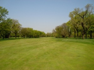 Wide view of a well-maintained golf course fairway lined with trees under a clear blue sky, showcasing a serene outdoor setting ideal for golfing.