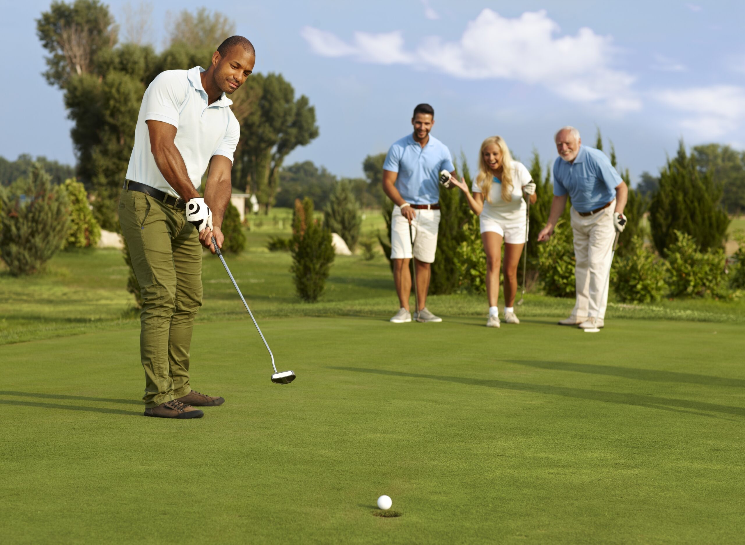 Male golfer putting in golf ball on the green, partners jittering